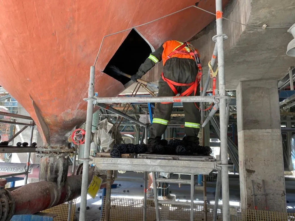 Trabajador con arnés en la boca de un equipo